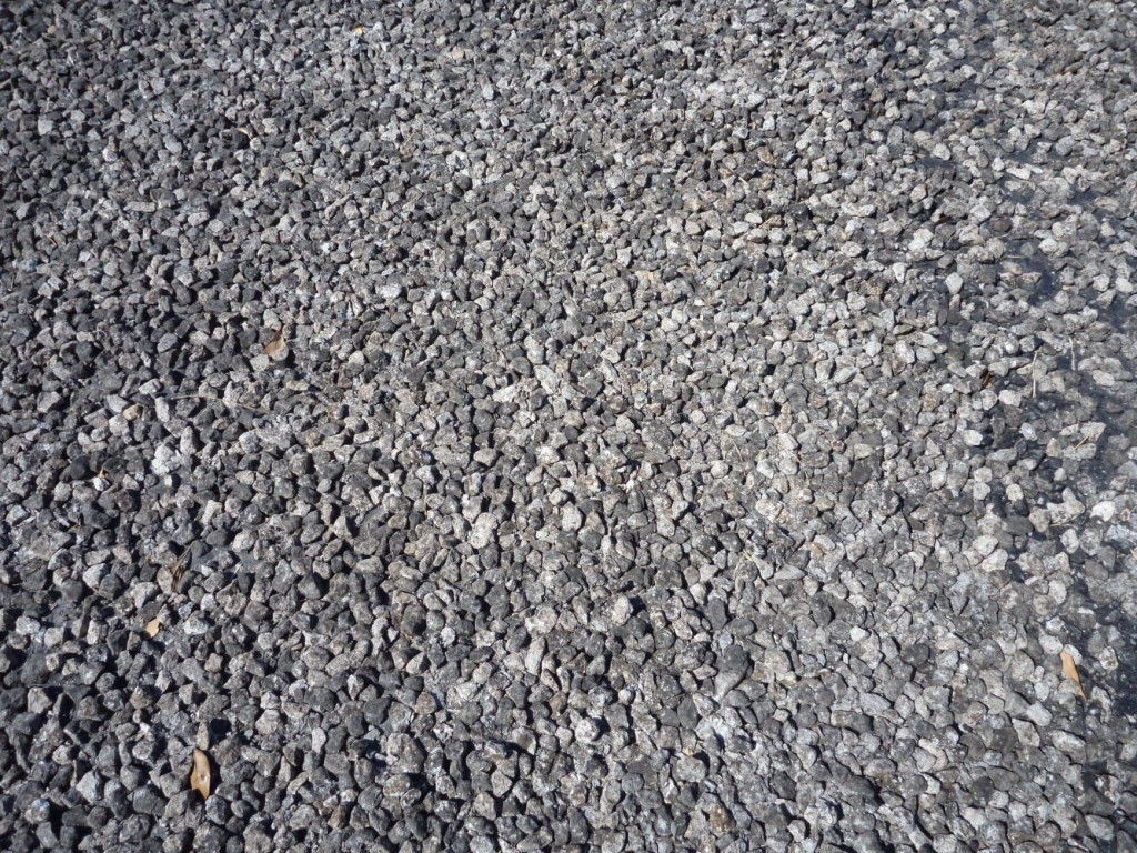 Chip-seal. Tar is spread out then pebbles/rocks thrown on top = cheap road. Most are the rocks are not loose. 