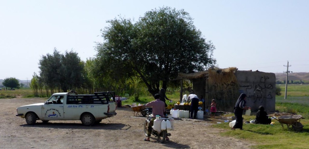 A typical fruit stand with a public fountain. People gather to fill their containers and picnic. 