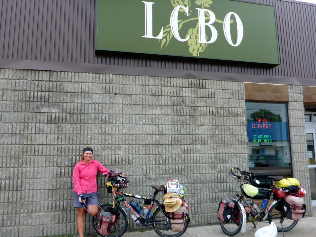 An LCBO near a campground with beer strapped to Jocelyn's bike and ice bought at a separate store. LCBO's are not allowed to sell ice.